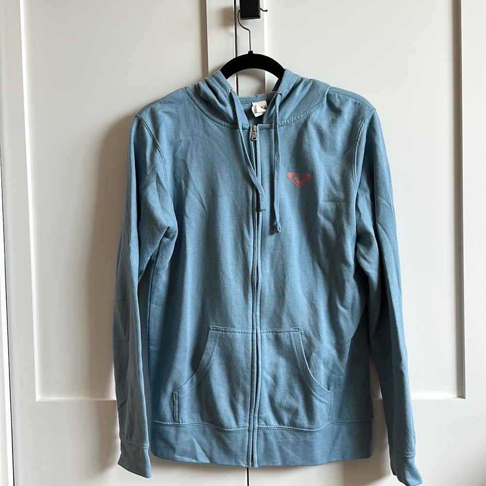 Light blue zip up jacket. Text: “See you in Manzanita”